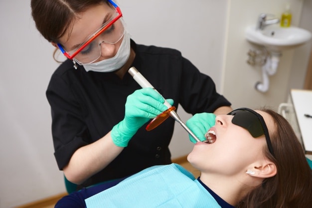 young-patient-black-goggles-getting-her-teeth-treated-by-female-hygienist-using-dental-curing-light_343059-402